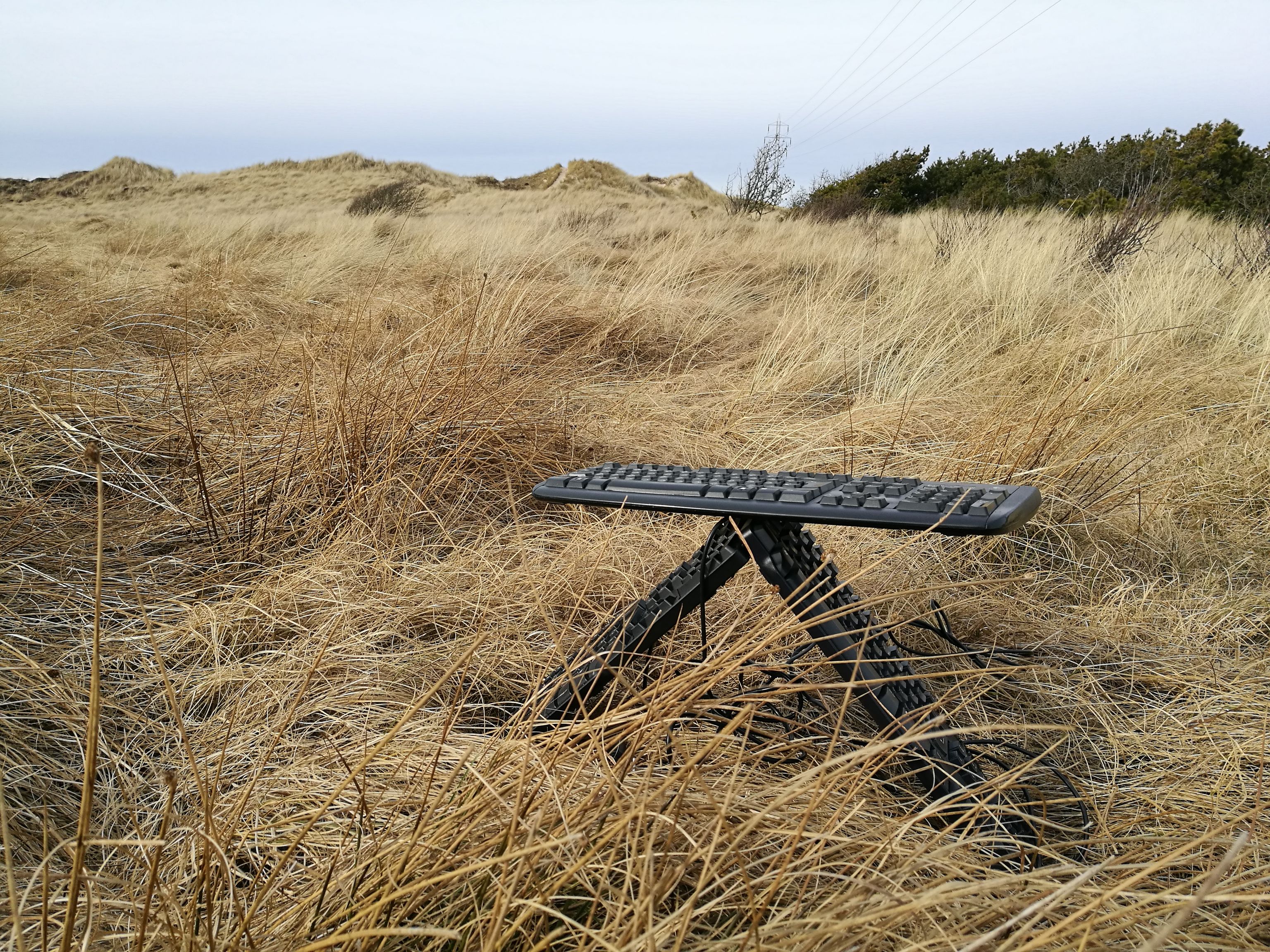 Two keyboards are placed next to each other. A third keyboard lies on this triangle. There are dunes in the background.